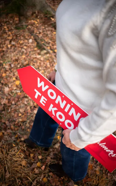 Vrouw met een plakaat waarop 'woning te koop' staat